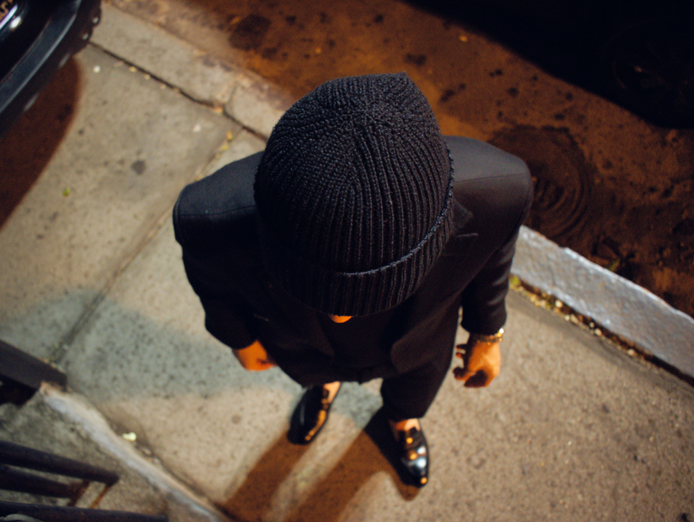 Man wearing Bay Clothing black ribbed knit beanie and dark outfit on city street at night, minimalist look