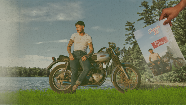 Man wearing a fitted white T-shirt and dark denim jeans sitting on a vintage motorcycle near a lake, holding a Bay Clothing poster in a nostalgic outdoor setting