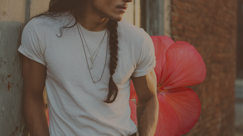 Men’s vintage white T-shirt styled with layered necklaces, heritage workwear vibe with soft natural lighting and red flower background